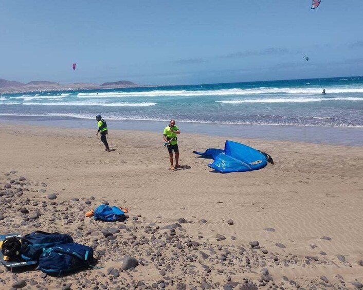 A beach with people, a deflated blue kite, and a surfboard. 5
