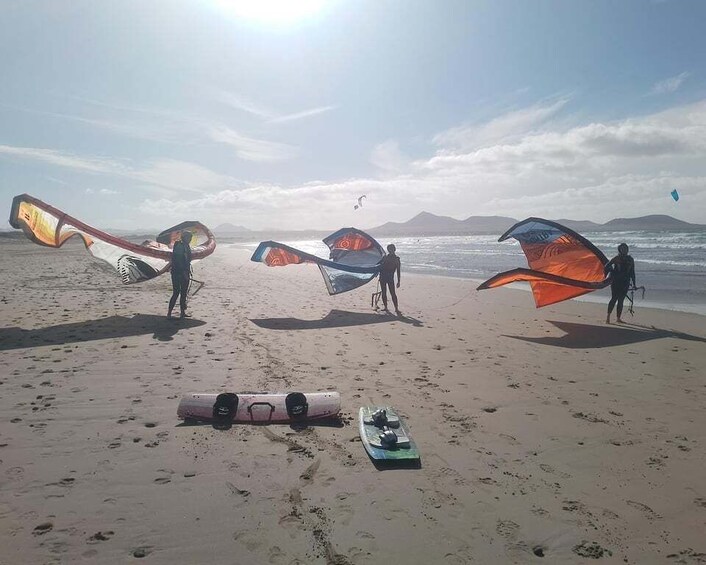 A beach with people holding kites and a surfboard on the sand. 2