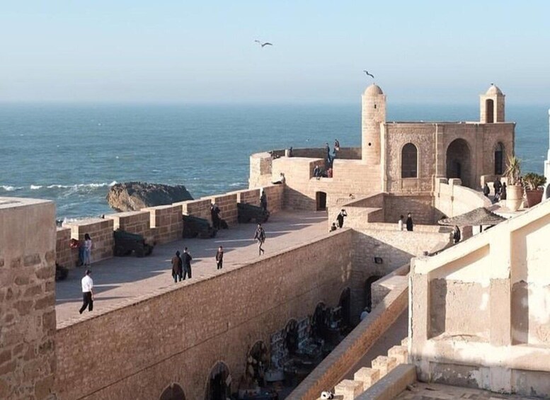 A coastal fortification with people walking around, overlooking the sea. 1