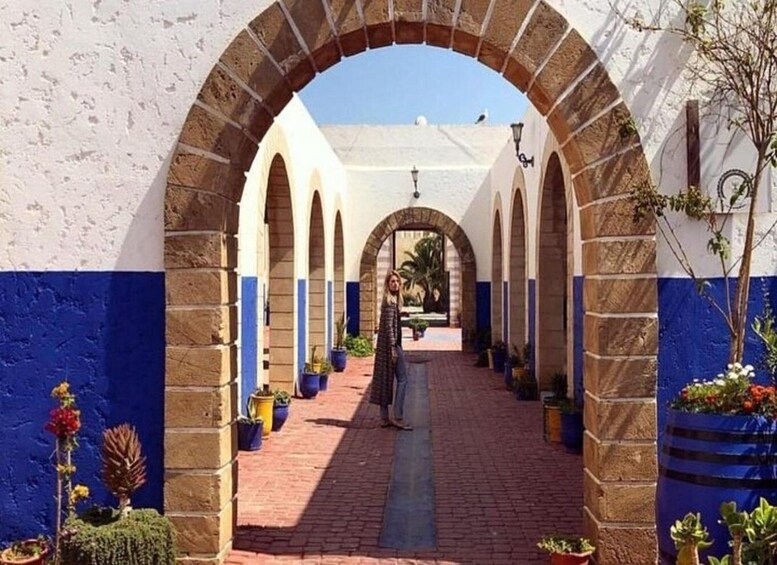 A corridor with arches, potted plants, and a person standing in the distance. 3