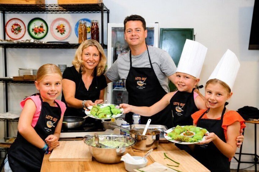 A group of people in a kitchen, some wearing chef hats, holding plates of food. 3