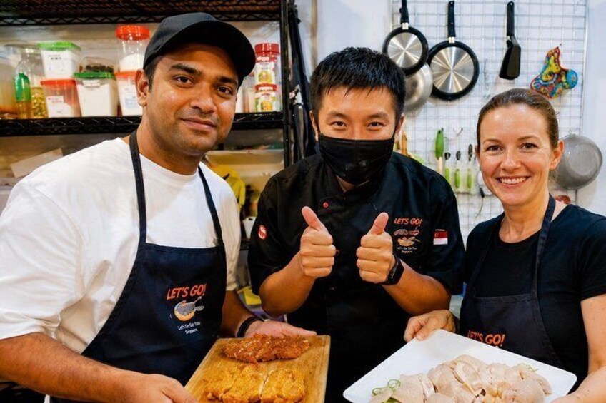 Three people in a kitchen, one holding a tray of food. 2