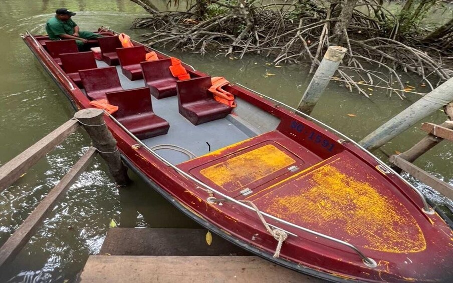 A red boat with orange seats docked at a pier, surrounded by water and vegetation. 3