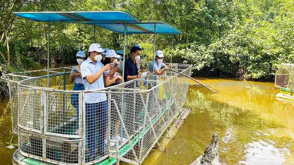A group of people on a boat with a cage structure, surrounded by water and greenery. 5