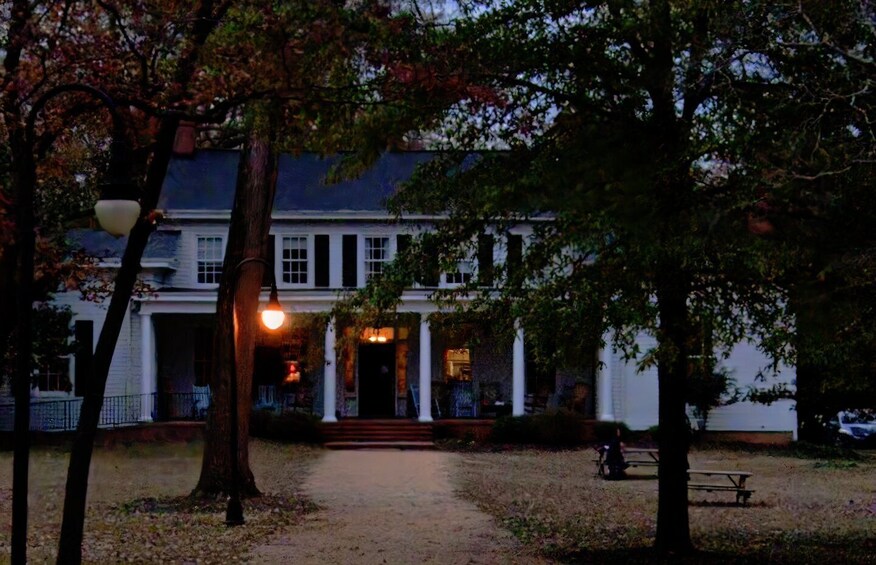 A large white building with a porch, surrounded by trees and a pathway. 1