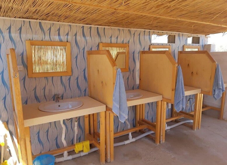 A rustic bathroom with wooden sinks and a straw roof. 3