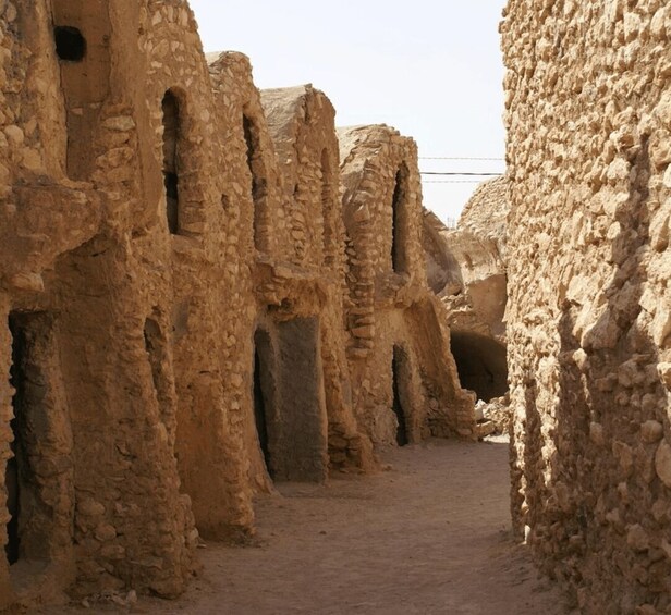 A narrow alley with ancient, weathered stone walls and arched doorways. 4