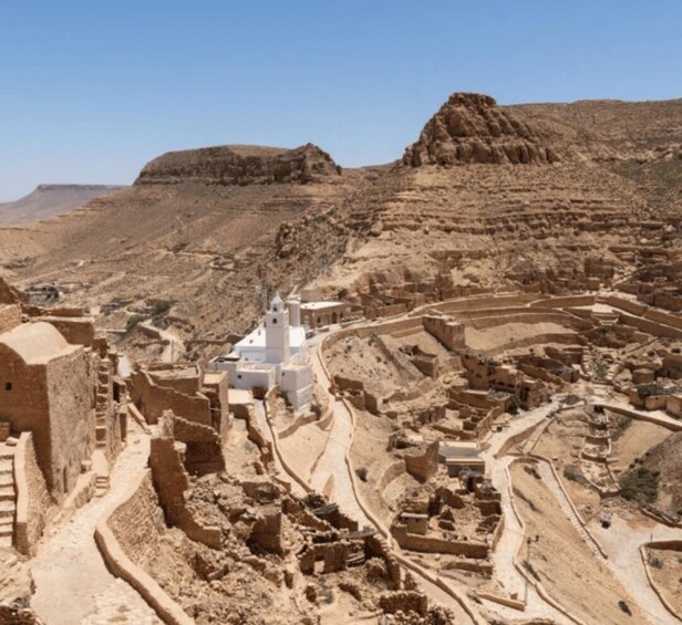 A desert landscape with ancient ruins and a white building with a minaret. 2