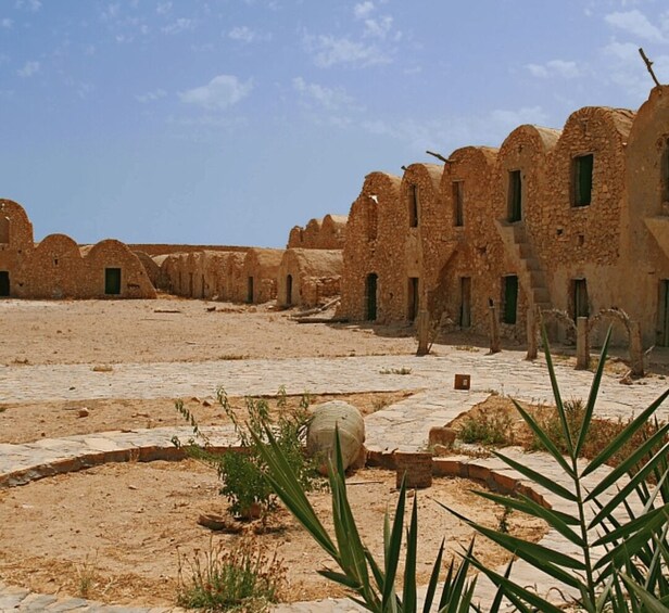 A desert landscape with ancient stone buildings, some with arched windows, and sparse vegetation. 1