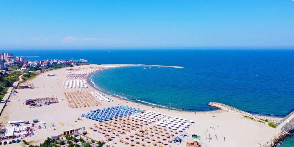 A coastal beach with umbrellas and sunbeds, a promenade, and buildings in the background. 2