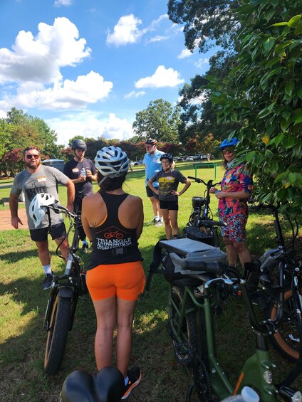 A group of people standing outdoors, some wearing helmets, with bicycles and an ATV nearby. 2