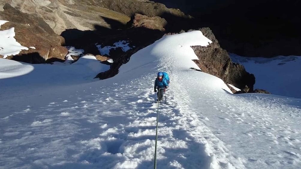 A person hiking on a snowy mountain trail with rocky outcrops. 2