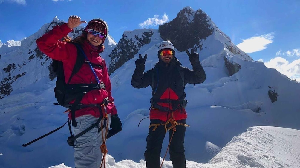 Two people in red jackets with backpacks on a snowy mountain peak. 1
