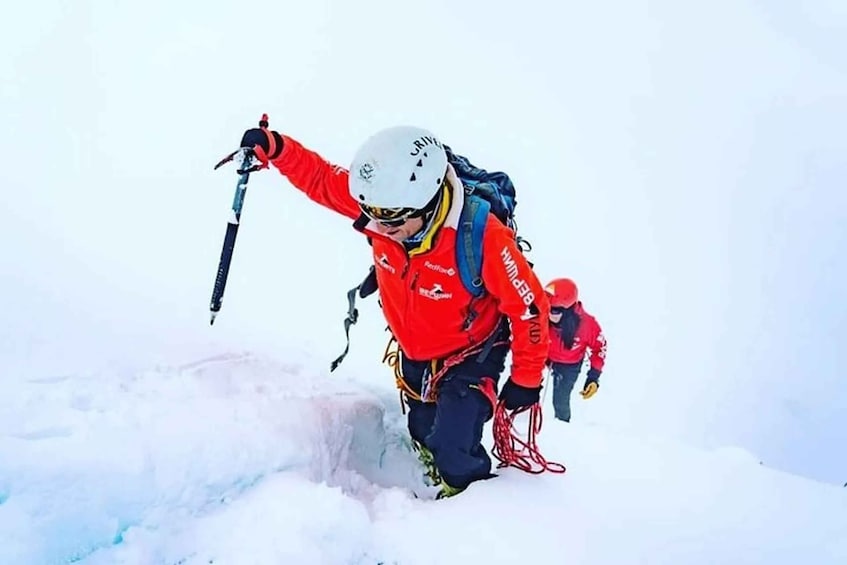 A person in a red jacket climbing a snowy slope with a child. 5