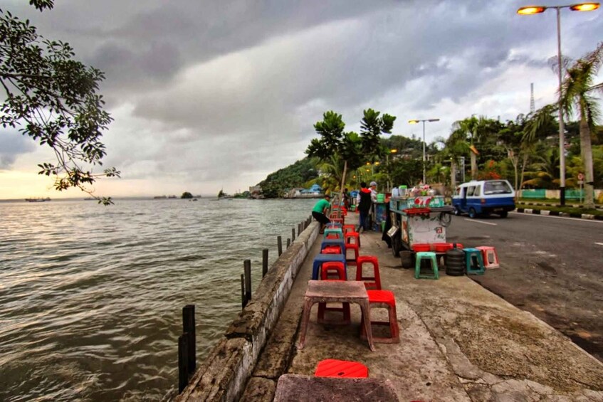 A waterfront with a row of colorful plastic stools and a blue vehicle parked on the road. 4