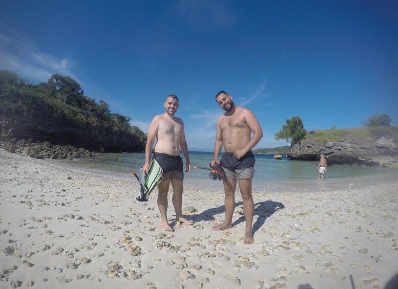 Two men on a sandy beach with rocky outcrops and clear blue water. 1