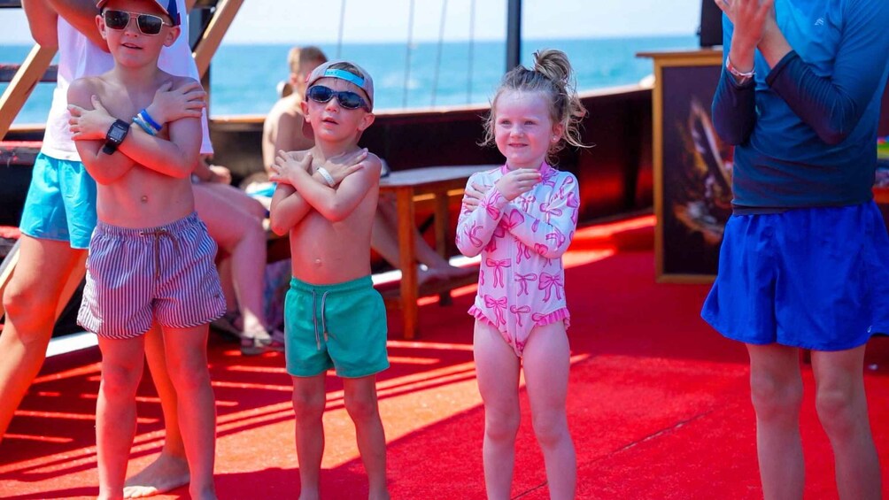 Children standing on a red carpet at a beachside event. 3