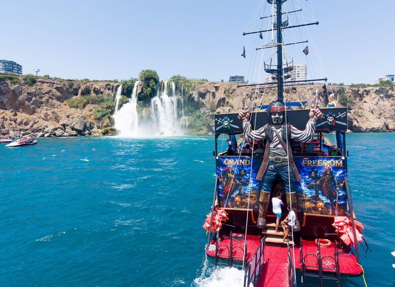 A pirate-themed boat with 'GRAND FREEDOM' written on the side, sailing near a waterfall. 1