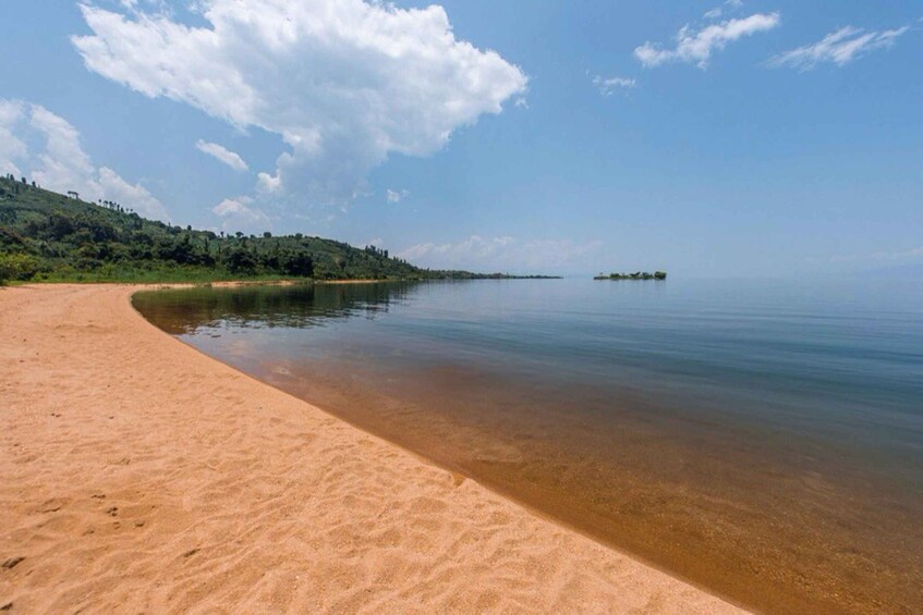 A sandy beach with clear water, a distant island, and a hilly landscape under a blue sky. 1