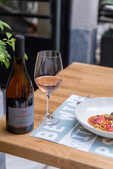 A bottle of wine, a glass of wine, and a plate of food on a wooden table. 1