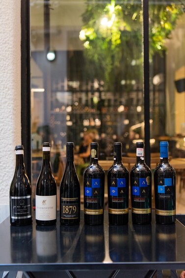A row of wine bottles on a table with a window view of a restaurant interior. 2