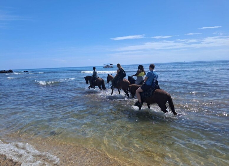 People riding horses through shallow water near a beach. 4