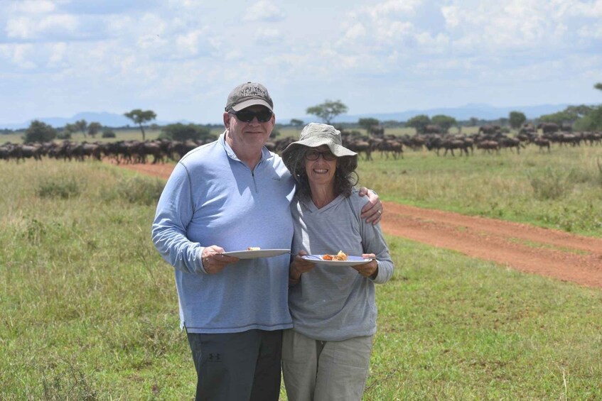 Two people standing in a grassy field with a herd of wildebeests in the background. 3