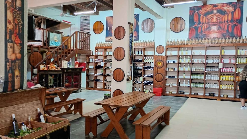 A wine shop with wooden tables and benches, wine bottles on shelves, and a staircase. 1