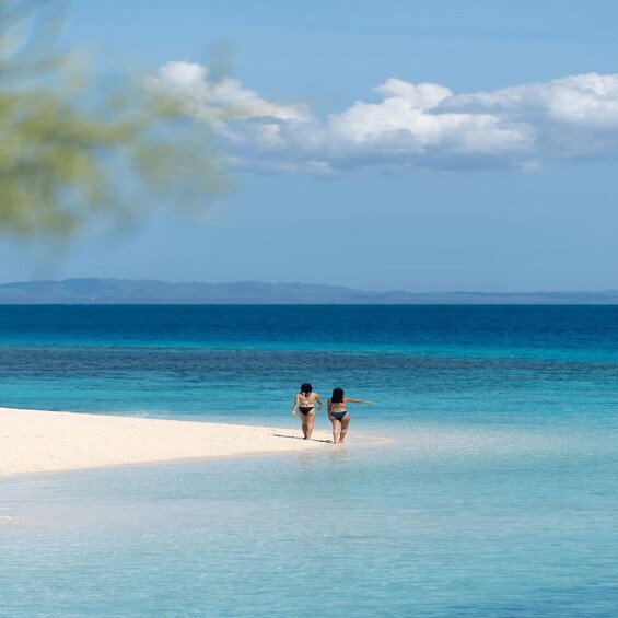 Two people walking on a white sandy beach with clear blue water and distant mountains. 4