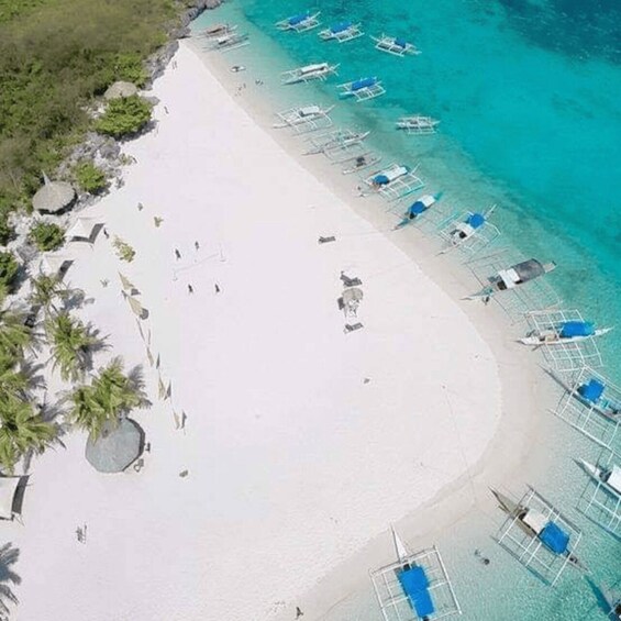 A beach with white sand, clear turquoise water, and several boats anchored near the shore. 1