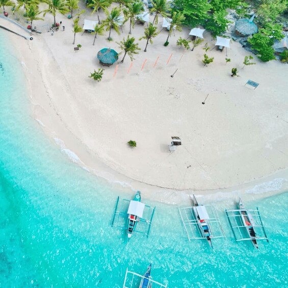 A beach with clear turquoise water, palm trees, and a few boats anchored near the shore. 2