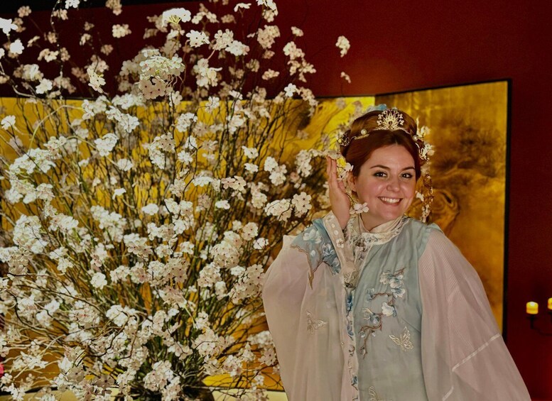A person in a dress with floral embroidery, standing in front of a large floral arrangement. 3