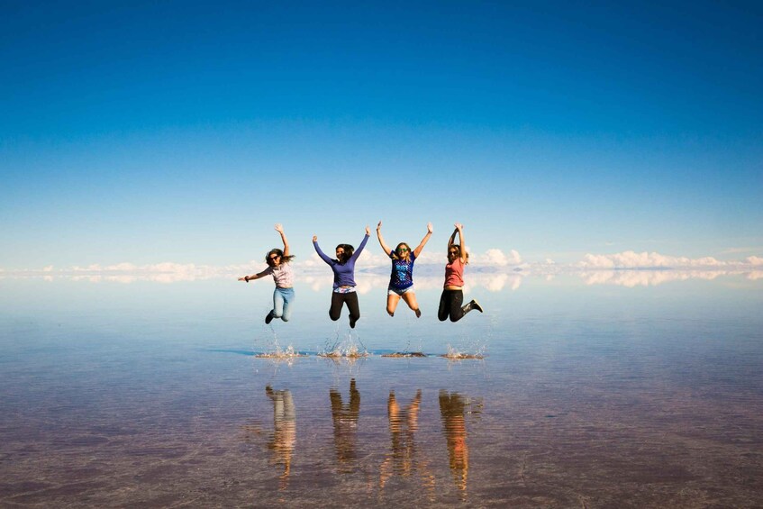 A group of people jumping in the air with a clear sky and calm water in the background. 1