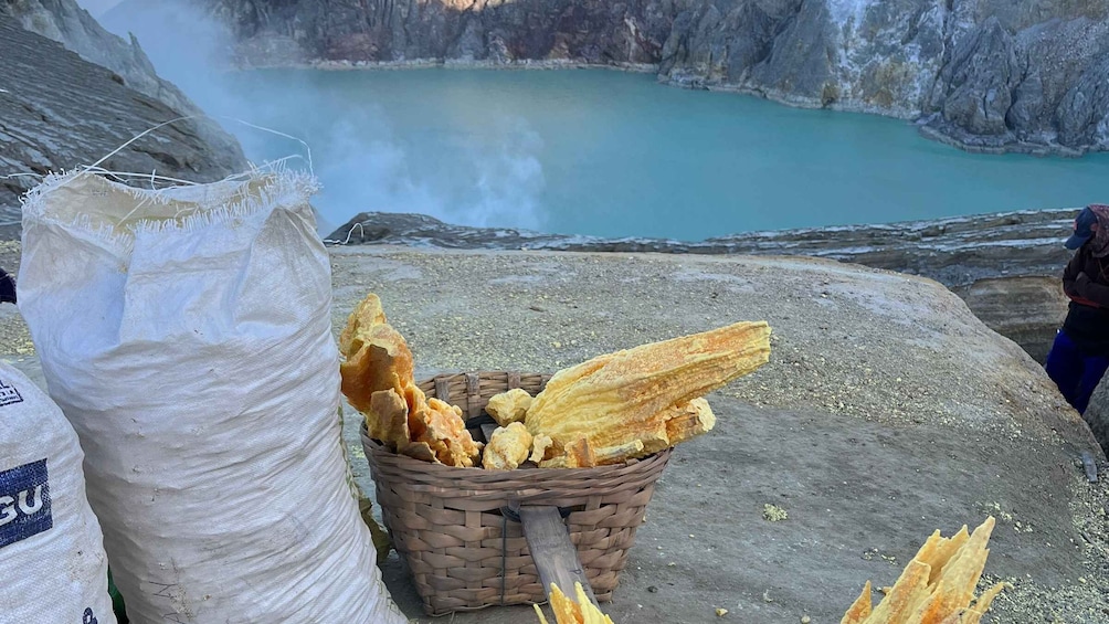 A basket of dried fish on a rocky shore with a large sack nearby. 5
