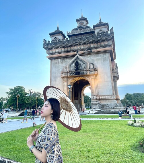 A woman with a parasol in front of an ornate historical gate. 3