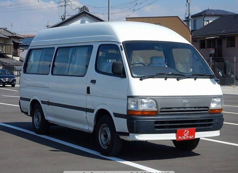 A white van parked in a lot with buildings and power lines in the background. 3