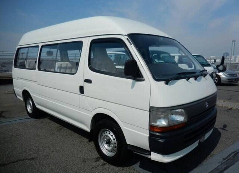 A white van parked in an open area with a clear sky and distant buildings. 4