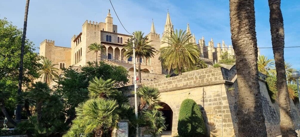 A historic building with a tower, palm trees, and a stone bridge. 1
