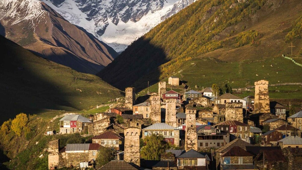 A historic village with stone buildings nestled in a valley, surrounded by mountains and a cross. 4