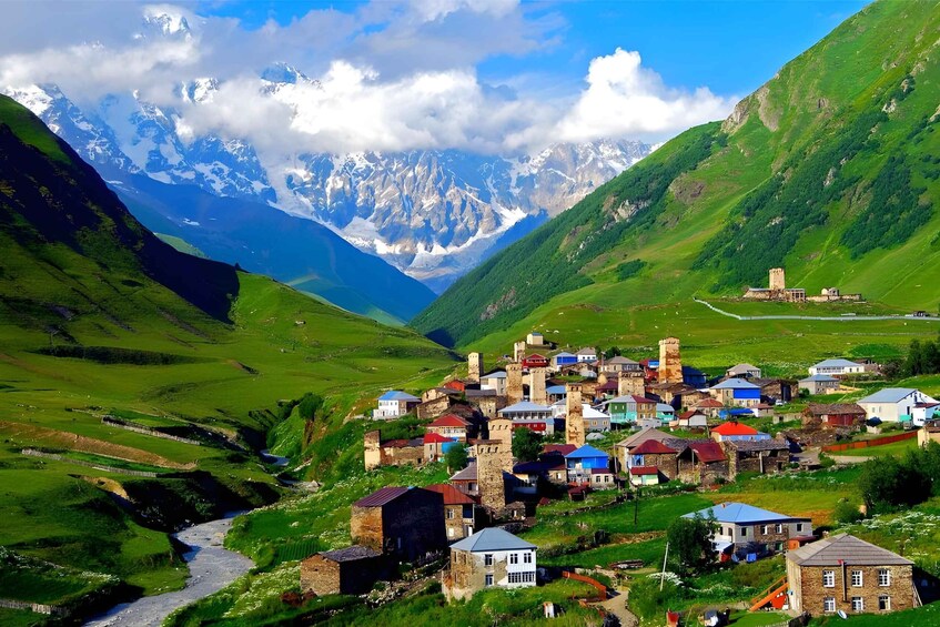 A village nestled in a valley with a castle, surrounded by mountains and greenery. 1