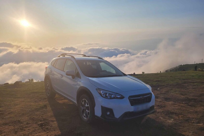 A white SUV parked on a grassy hill with clouds below and the sun shining in the background. 3