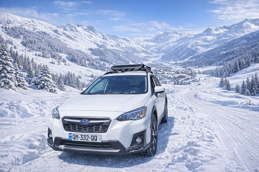 A white SUV on a snow-covered mountain road with snow-covered trees and mountains in the background. 2