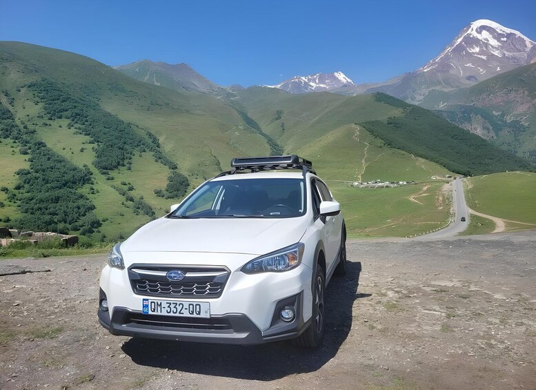 A white SUV parked on a dirt road with a mountainous landscape in the background. 5