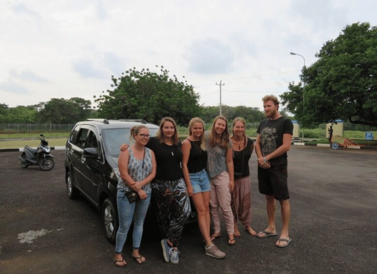 A group of people standing in a parking lot with a black car and a scooter in the background. 2
