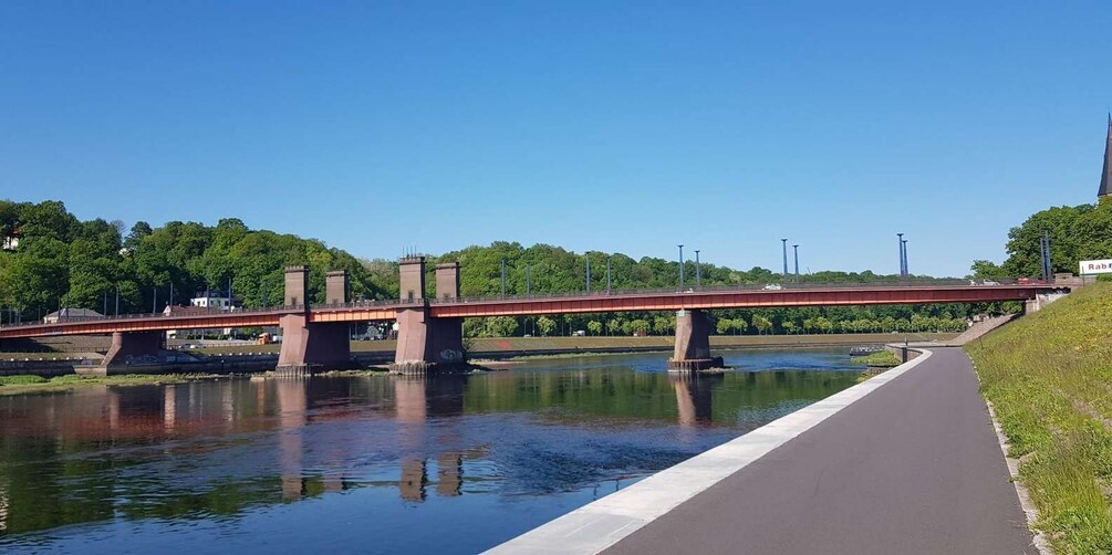 A red bridge over a calm river with a paved walkway on the right. 1