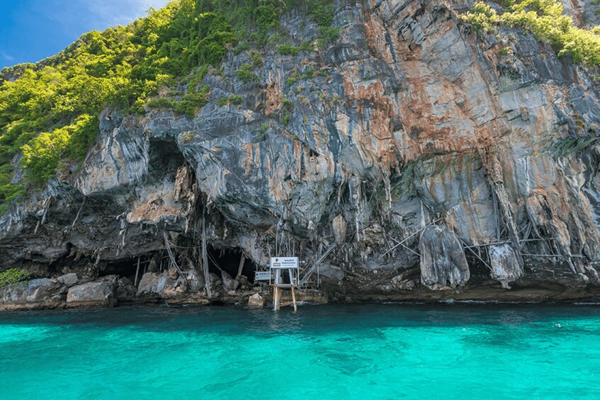 A rocky cliff with a cave entrance and a lifeguard stand by the water. 4