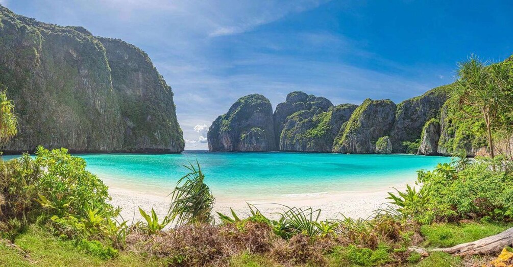 A beach with clear turquoise water, surrounded by lush greenery and limestone cliffs. 2