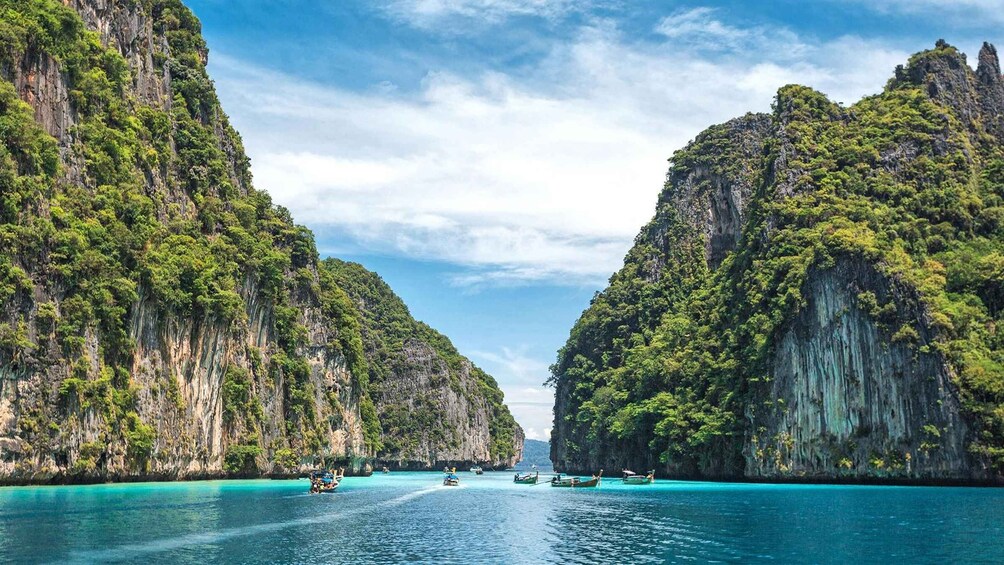 A turquoise sea flanked by steep, forested cliffs with boats in the water. 1