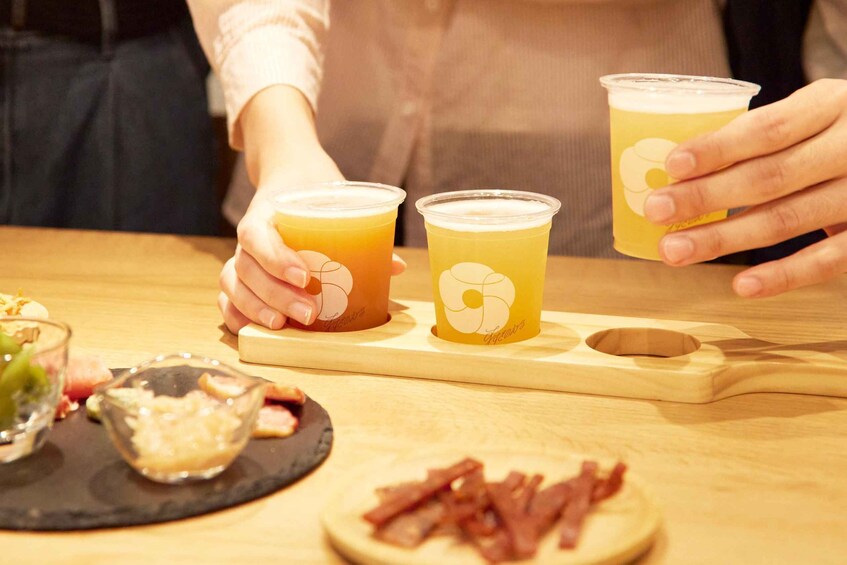 Two people holding cups with a logo, a wooden board with food items, and a wooden table. 2
