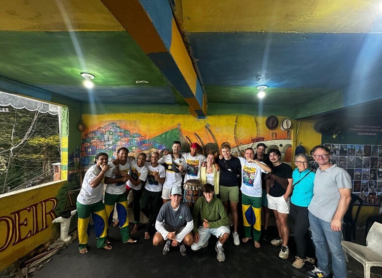 A group of people posing in a colorful, painted room with murals and a window overlooking greenery. 5